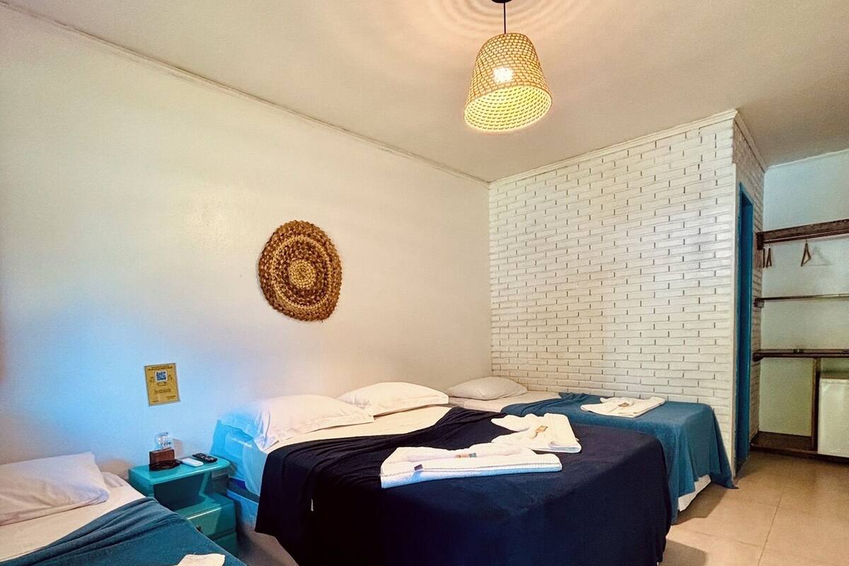 Habitación de hotel con dos camas, pared de ladrillo blanco, tapiz tejido y lámpara colgante.