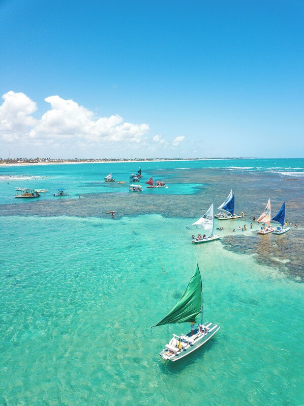 A coastal area with clear turquoise waters, boats, and a distant shoreline. - Brisa do Porto Pousada (Ipojuca)