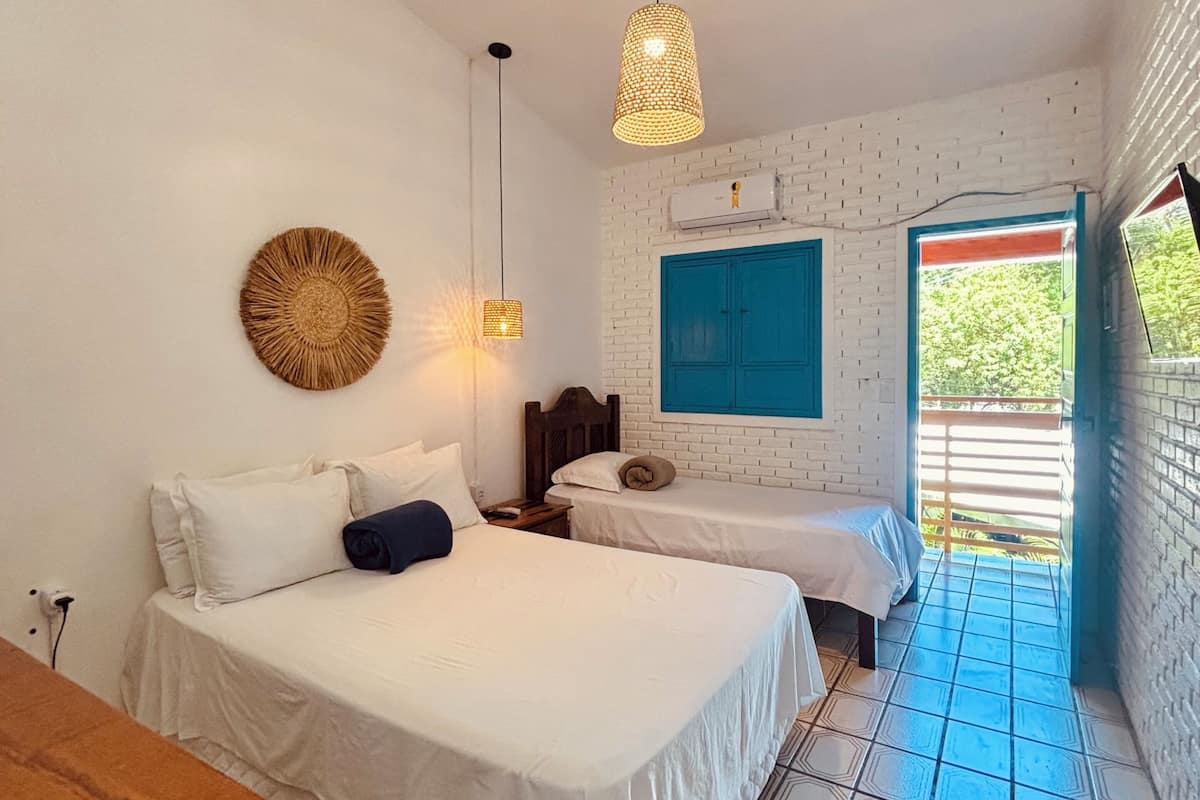 Una habitación con dos camas, una mesa de madera, aire acondicionado de pared y vistas a zonas verdes por una ventana.