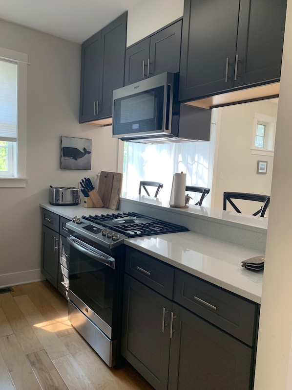 A modern kitchen with dark cabinets, stainless steel appliances, and a large window providing natural light.