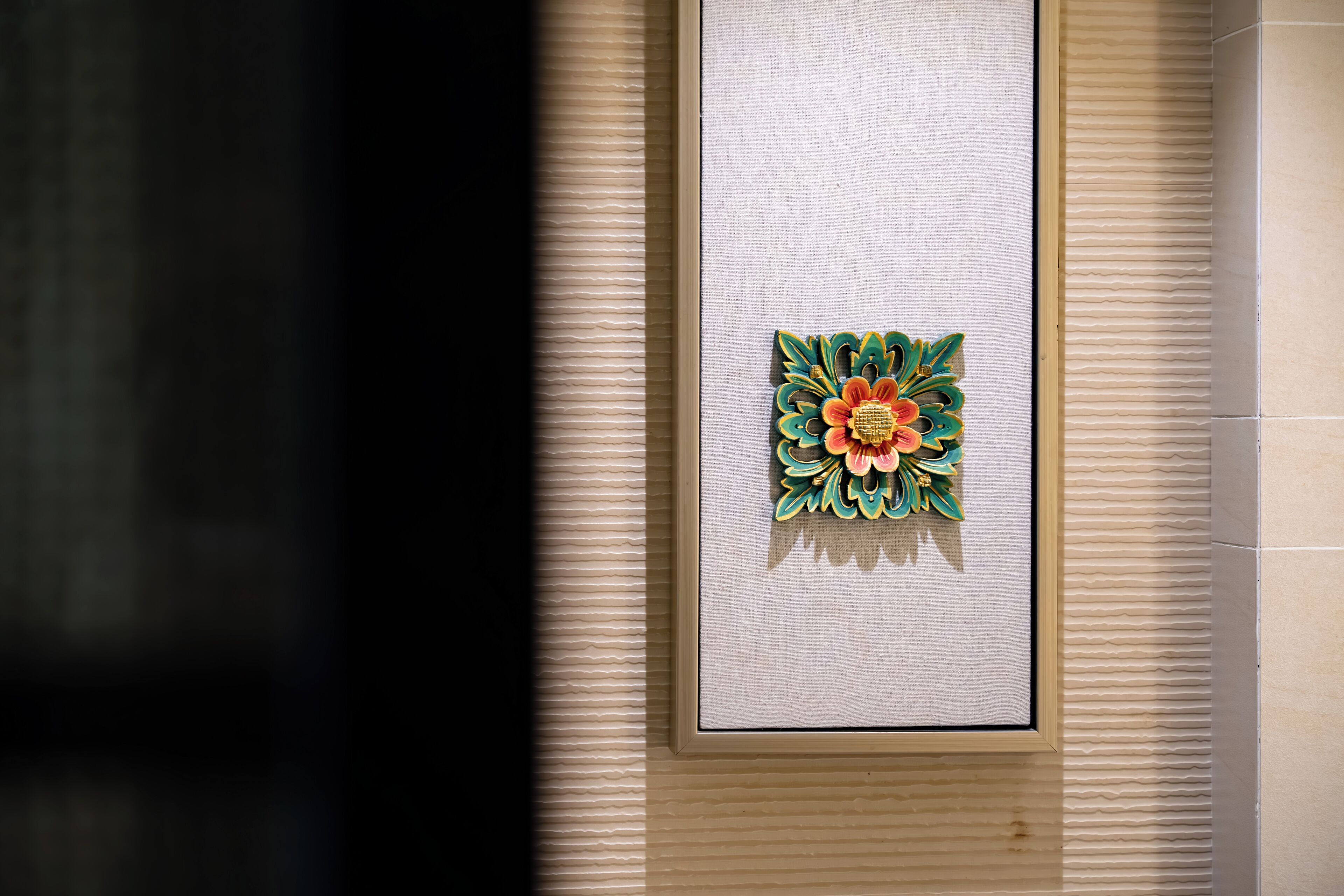 A framed artwork of a colorful flower on a textured wall.