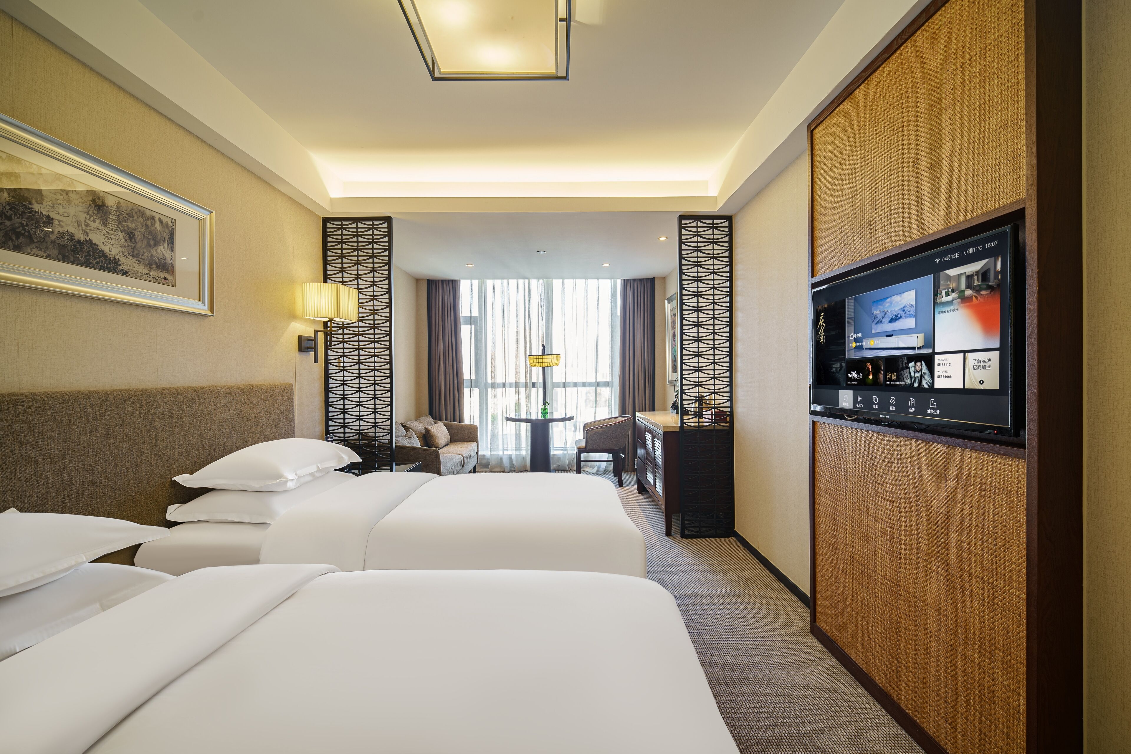 A hotel room with two beds, a desk, a TV, and a view of the city.