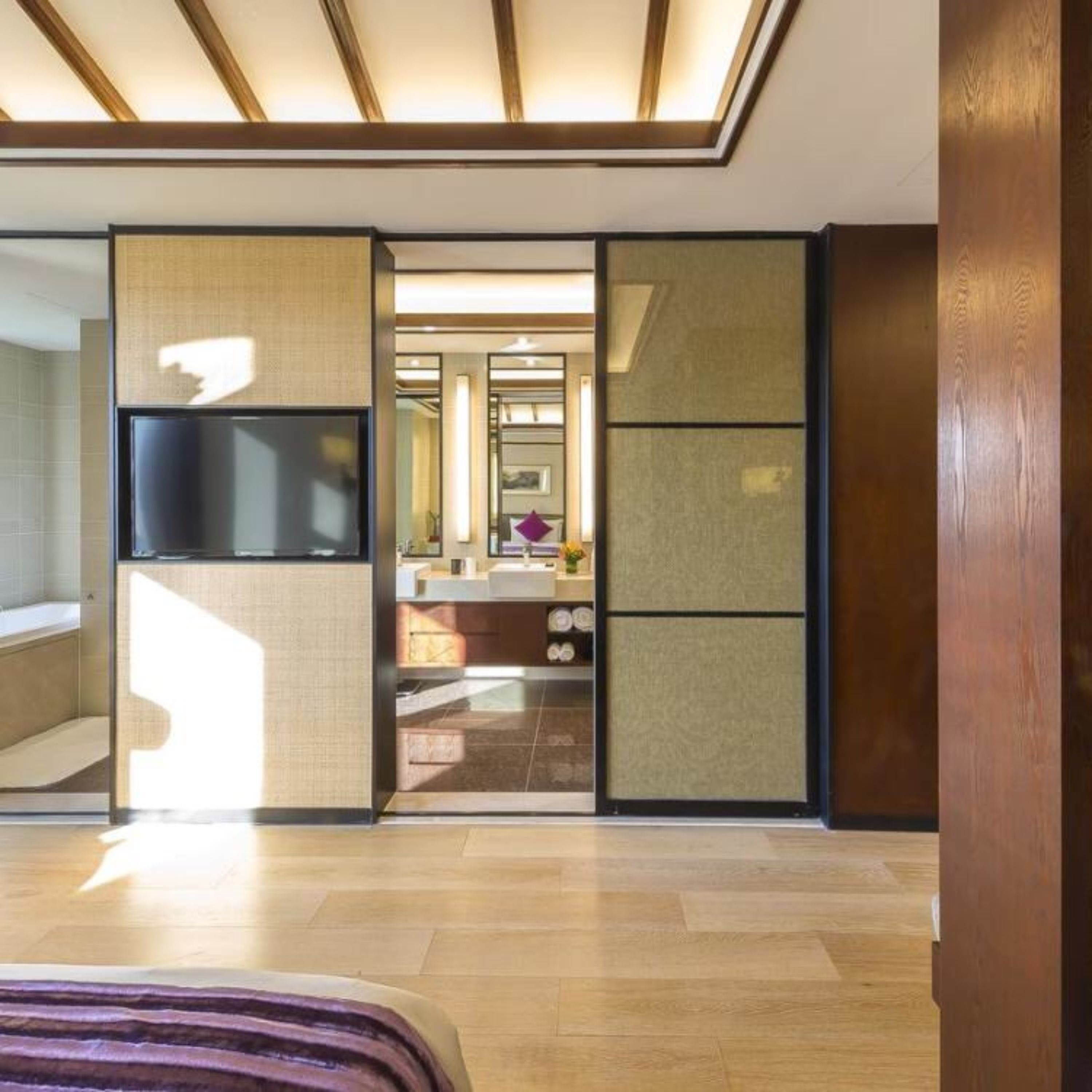Ein modernes Hotelzimmer mit einem großen Bett, einem Fernseher und einer Schiebetür zu einem Badezimmer und einer Küchenzeile.