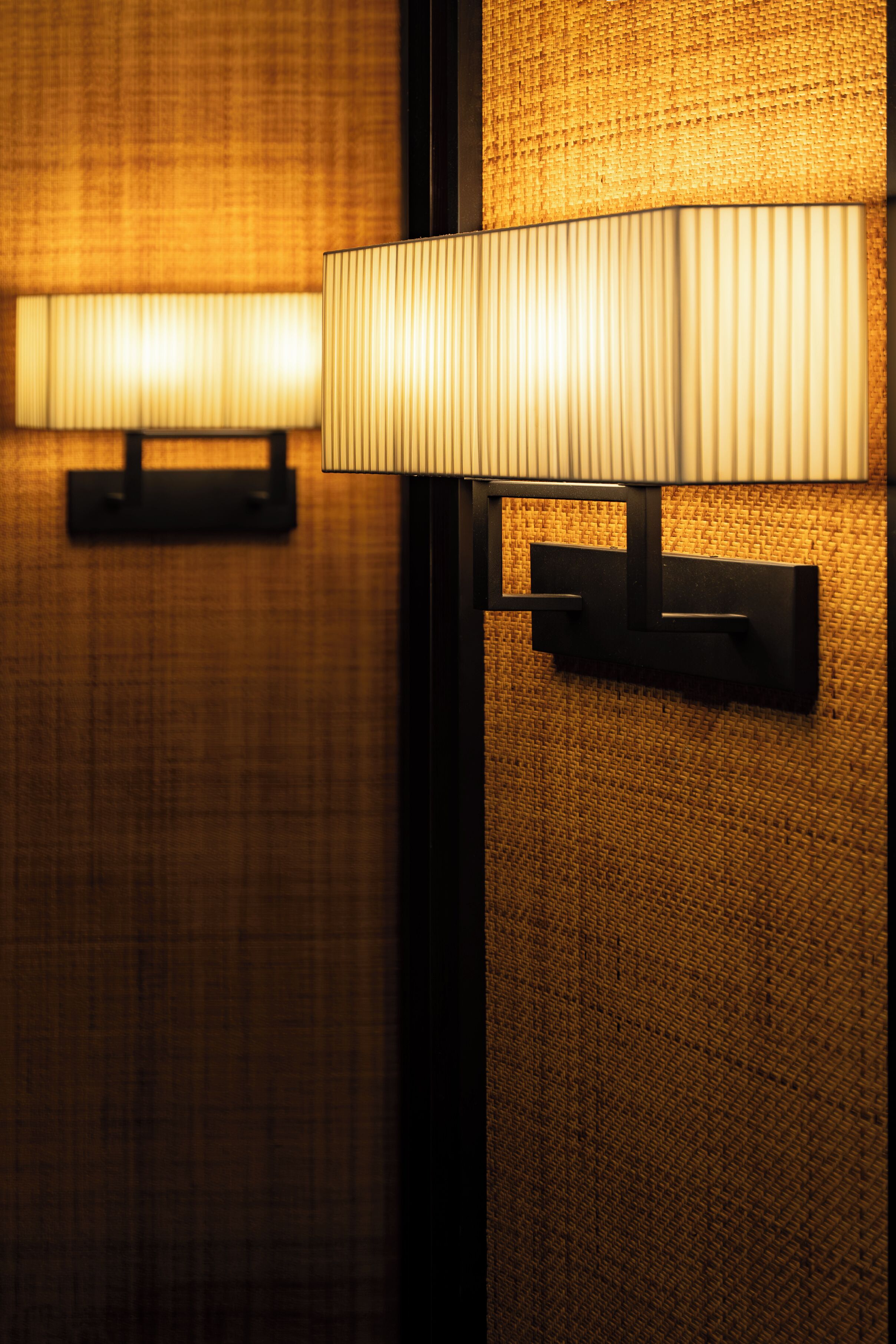 A wall-mounted lamp with a rectangular base and a pleated shade.