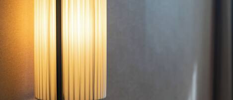 A modern table lamp with a cylindrical shade and a rectangular base, placed on a reflective surface.