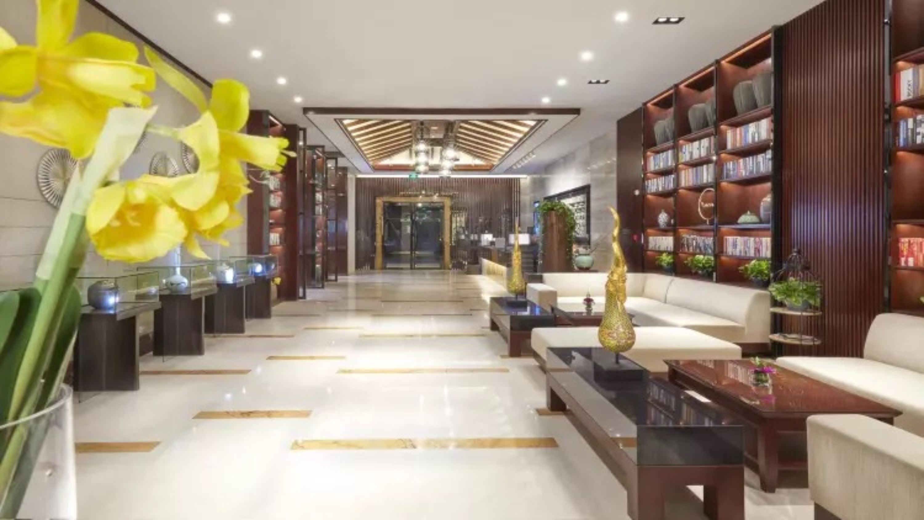 A modern lobby with a central seating area, a reception desk, and a bookshelf filled with books.