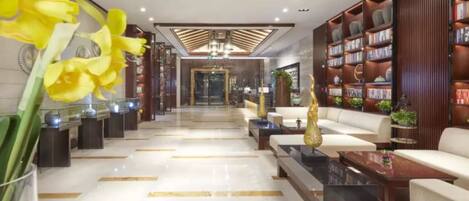 A modern lobby with a central seating area, a reception desk, and a bookshelf filled with books.