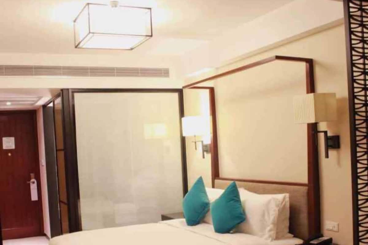 A hotel room with a large bed, a nightstand, a lamp, and a view of the outside.
