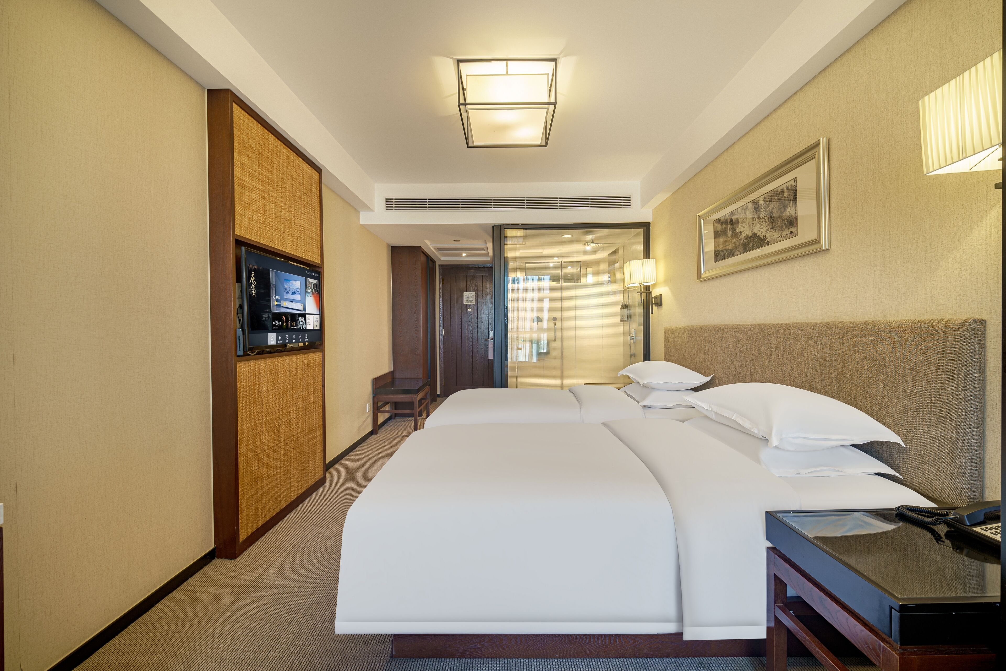 Une chambre d’hôtel avec un grand lit, un bureau avec un téléphone, une télévision et un tableau encadré au mur.