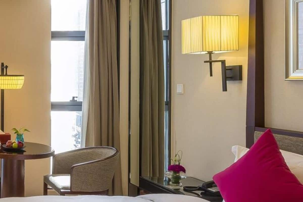 A hotel room with a bed, a desk, a chair, a lamp, and a window with curtains.