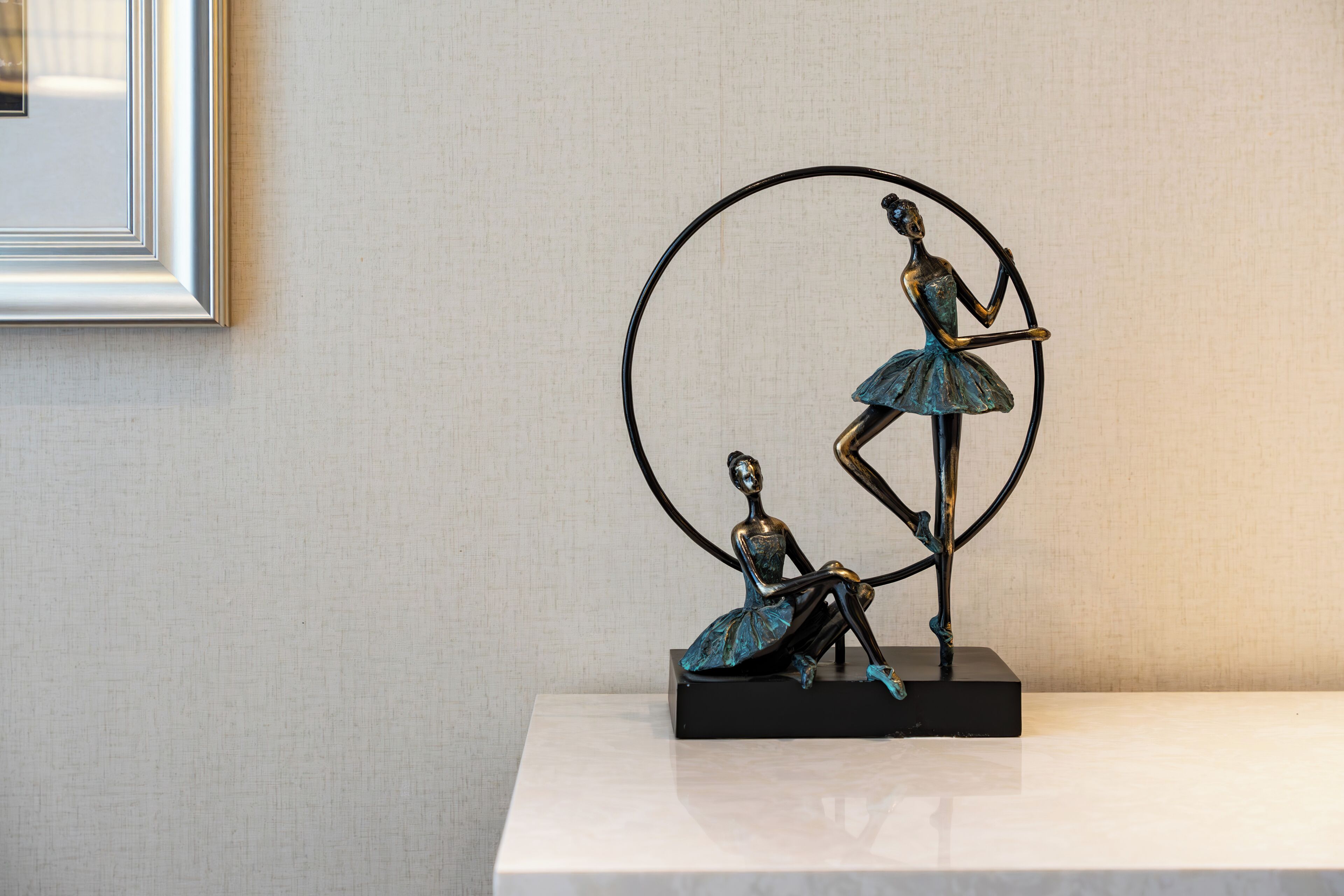 Una escultura de dos figuras sobre un pedestal negro, frente a una pared lisa.