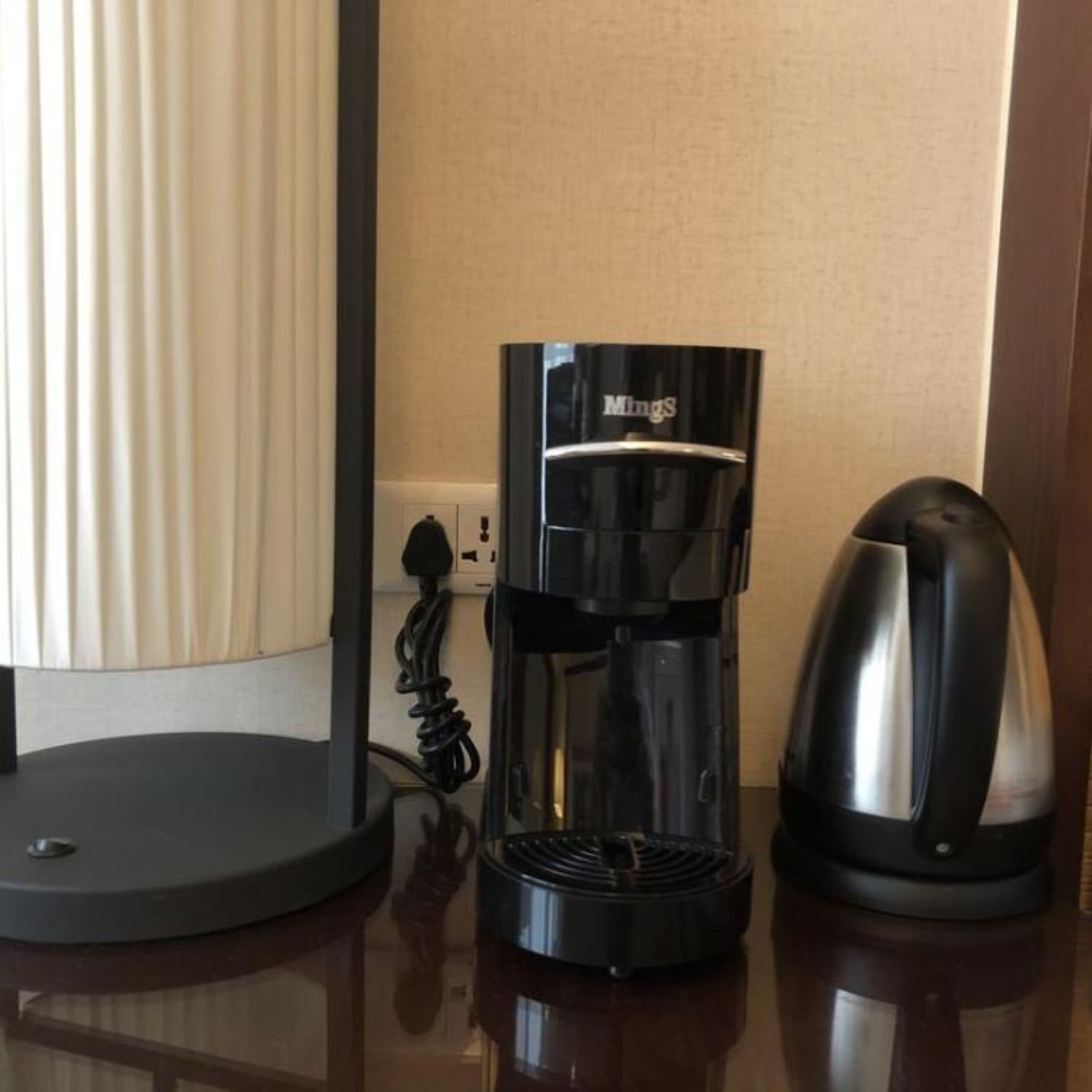 A coffee maker, a kettle, and a power outlet on a wooden surface.