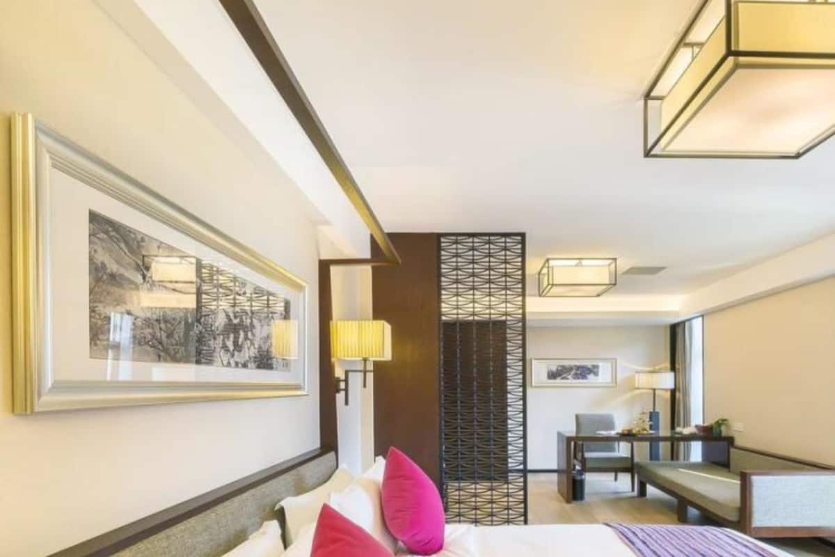 A hotel room with a large bed, two pillows, a desk, a chair, and a decorative partition.