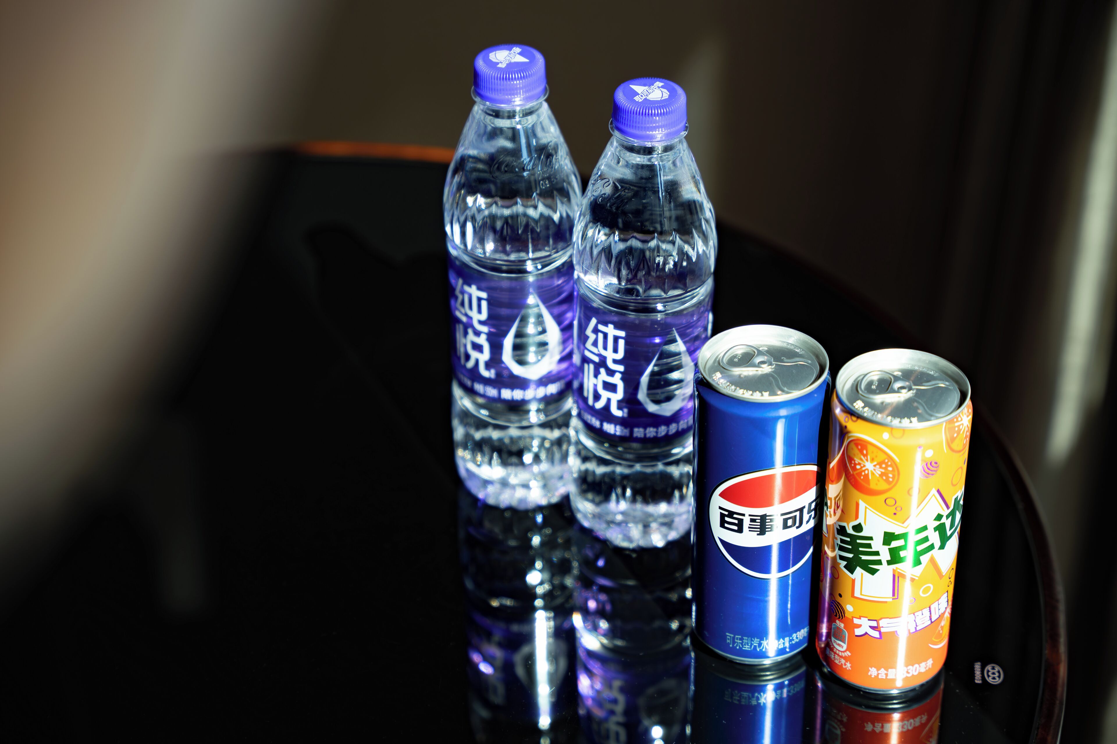 Dos botellas de agua y dos latas sobre una superficie reflectante.