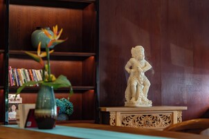 Una estatua sobre un pedestal, una estantería con libros y un florero con una planta.