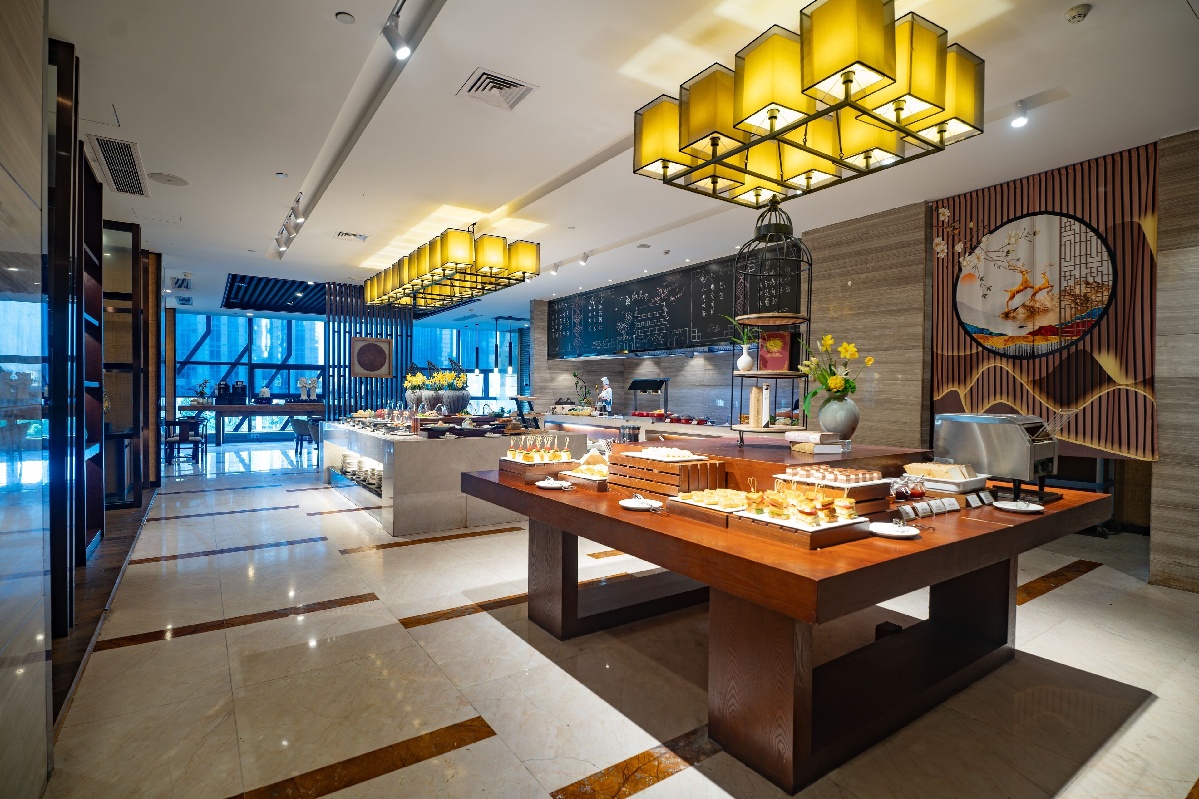 A modern hotel lobby with a buffet area, large windows, and contemporary lighting fixtures.