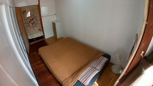 A small, compact room with a single bed, a small desk, and a fan. - Guesthouse & Diving Seacolo (Ishigaki)