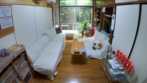 A cozy room with a sofa, a small table, and a refrigerator. There is a fan on the wall and a window providing natural light. - Guesthouse & Diving Seacolo (Ishigaki)