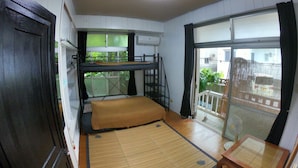 A compact room with a bunk bed, a tatami mat, a small table, and a sliding door leading to a balcony. - Guesthouse & Diving Seacolo (Ishigaki)