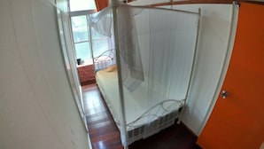 A room with a bed, a window with curtains, a wooden floor, and an orange wall. - Guesthouse & Diving Seacolo (Ishigaki)
