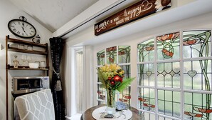 A cozy room with a clock, a shelf with glasses, a vase with flowers, and a window with stained glass. - Adams Guest Full House, King Williams Area, Southtown (San Antonio)