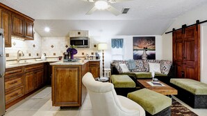 A spacious living area with a sofa, ottoman, and a dining table. A kitchen with wooden cabinets and a microwave is visible. - Adams Guest Full House, King Williams Area, Southtown (San Antonio)