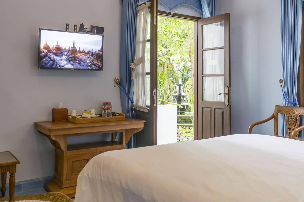A bedroom with a bed, a television mounted on the wall, a wooden nightstand, and a window with curtains.