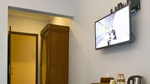 Una habitación con un escritorio de madera, un televisor montado en la pared, un armario de madera y una alfombra estampada en el suelo.