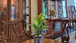 Un comedor con sillas de madera y una mesa redonda, una planta en maceta y un aparador decorativo con puertas de cristal.