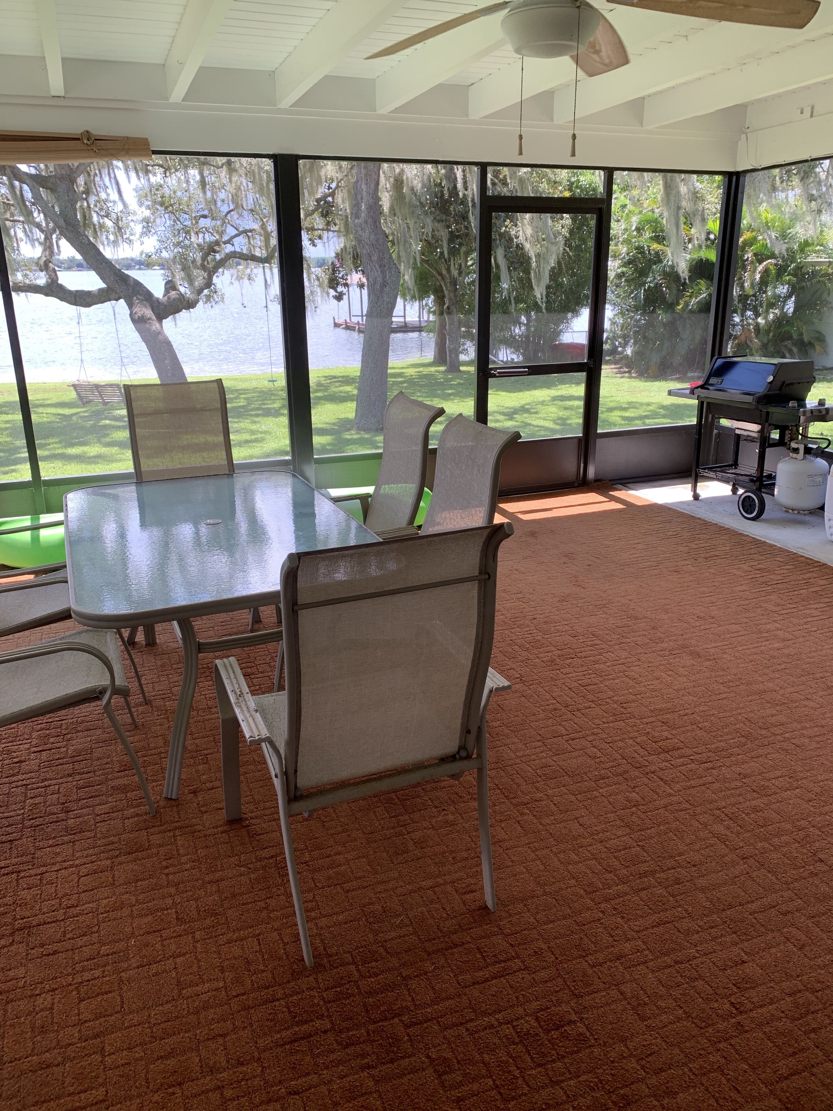 A room with a large table and chairs, a ceiling fan, and a view of a lake and trees.