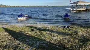 Scena con un lago, due jet ski sull'acqua e un pontile con un gazebo e la bandiera americana.