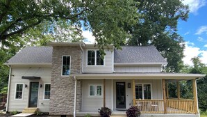 A two-story house with a stone facade, a front porch, and a covered deck.