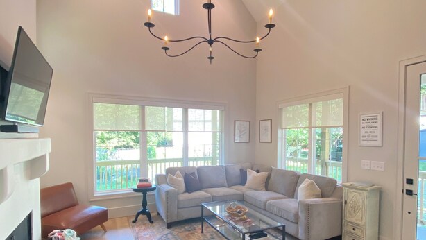A spacious living room with a high ceiling, a chandelier, a fireplace, and large windows.