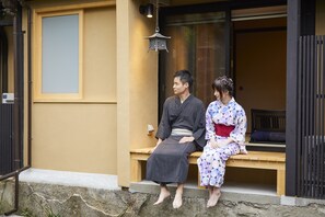 Two people sitting on a wooden bench outside a building with a traditional Japanese lantern above them.