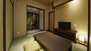 A traditional Japanese room with tatami flooring, a low table, a television, and a sliding door leading to a garden. - Rinn Tsukinuke (Kyoto)