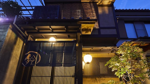 A traditional Japanese building with a wooden entrance gate, a stone pathway leading to the entrance, and a small garden with rocks and plants. - Rinn Tsukinuke (Kyoto)