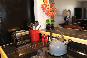 A kitchen counter with a toaster, a kettle, a red spice rack, and a vase with flowers.