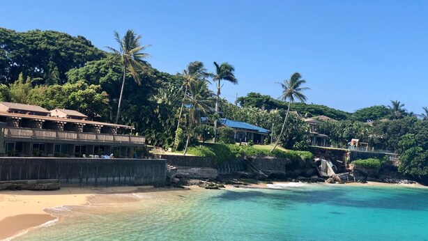 A beachfront property with a wooden building, a concrete barrier, and a clear turquoise sea.