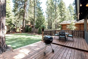 Eine Holzterrasse mit Grill, Sitzgelegenheiten und Blick auf ein bewaldetes Gebiet.