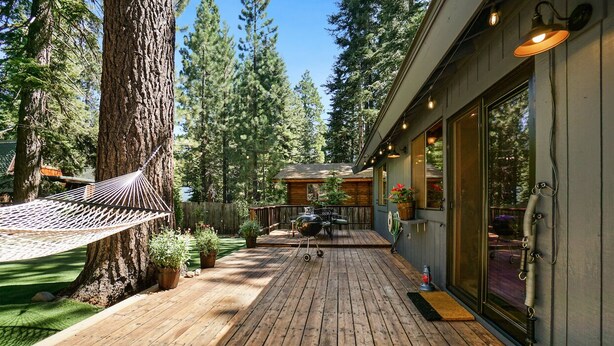 Une terrasse en bois avec un hamac, un barbecue et une porte vitrée donnant sur un espace extérieur abrité.