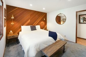 Ein Schlafzimmer mit einem großen Bett, einem Holzkopfstück, Nachttischlampen, einem runden Spiegel und einem gerahmten Bild an der Wand.
