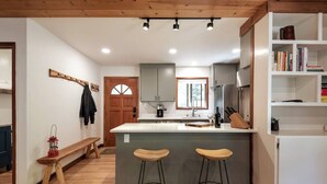 Une cuisine moderne dotée d’un îlot central, de tabourets de bar en bois, d’une machine à café et d’une bibliothèque.