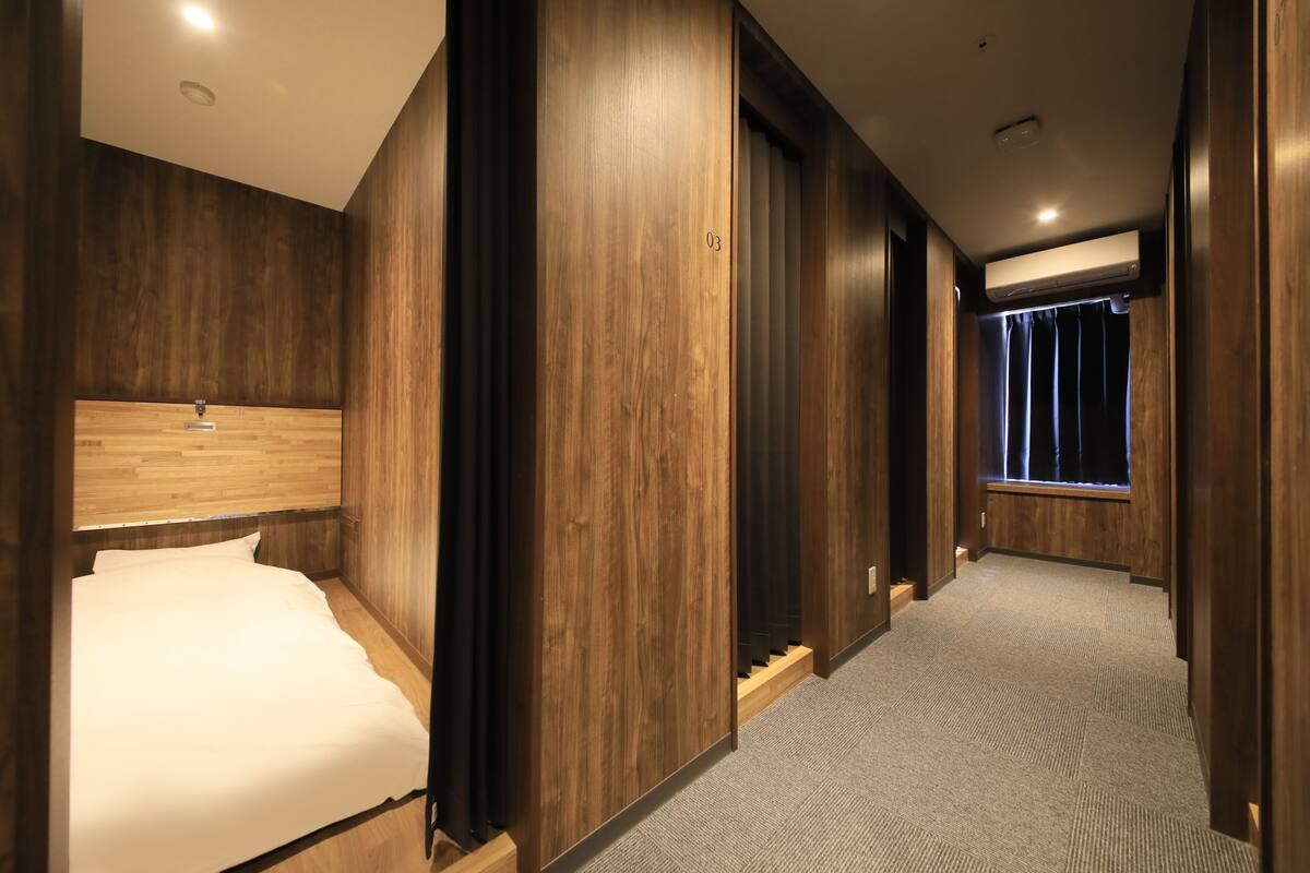 A hotel room with a wooden headboard, a bed, a built-in wardrobe, and a window with curtains.