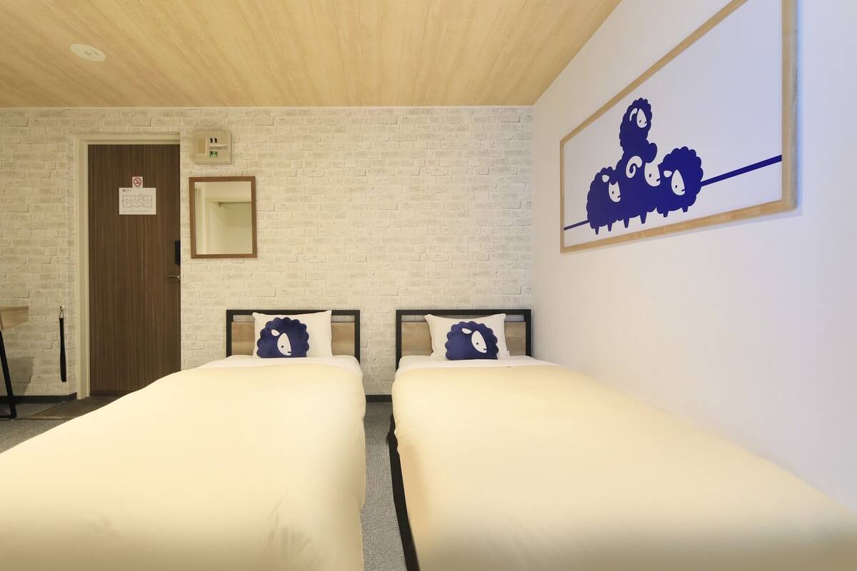 A hotel room with two beds, a desk with a chair, a television, a brick-patterned wall, and a framed picture on the wall.