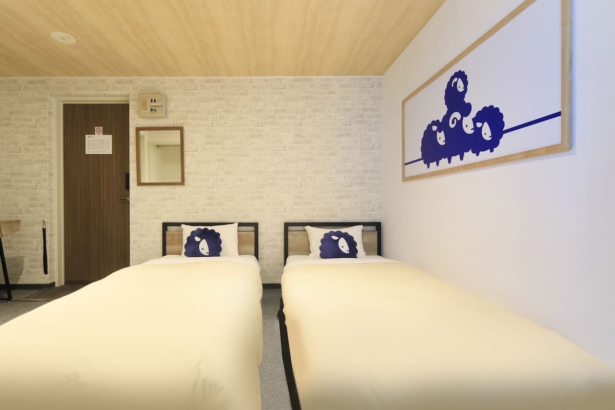 Une chambre d’hôtel avec deux lits, un bureau avec une chaise, une télévision, un mur décoré d’un motif en briques et un tableau encadré accroché au mur.