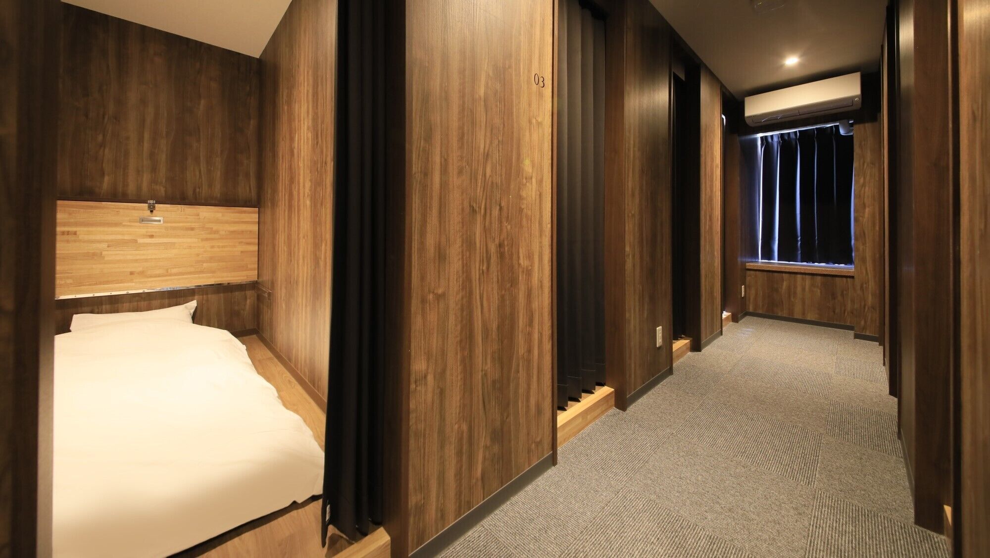 A hotel room with a wooden headboard, a bed, a carpeted hallway, and a window with curtains.