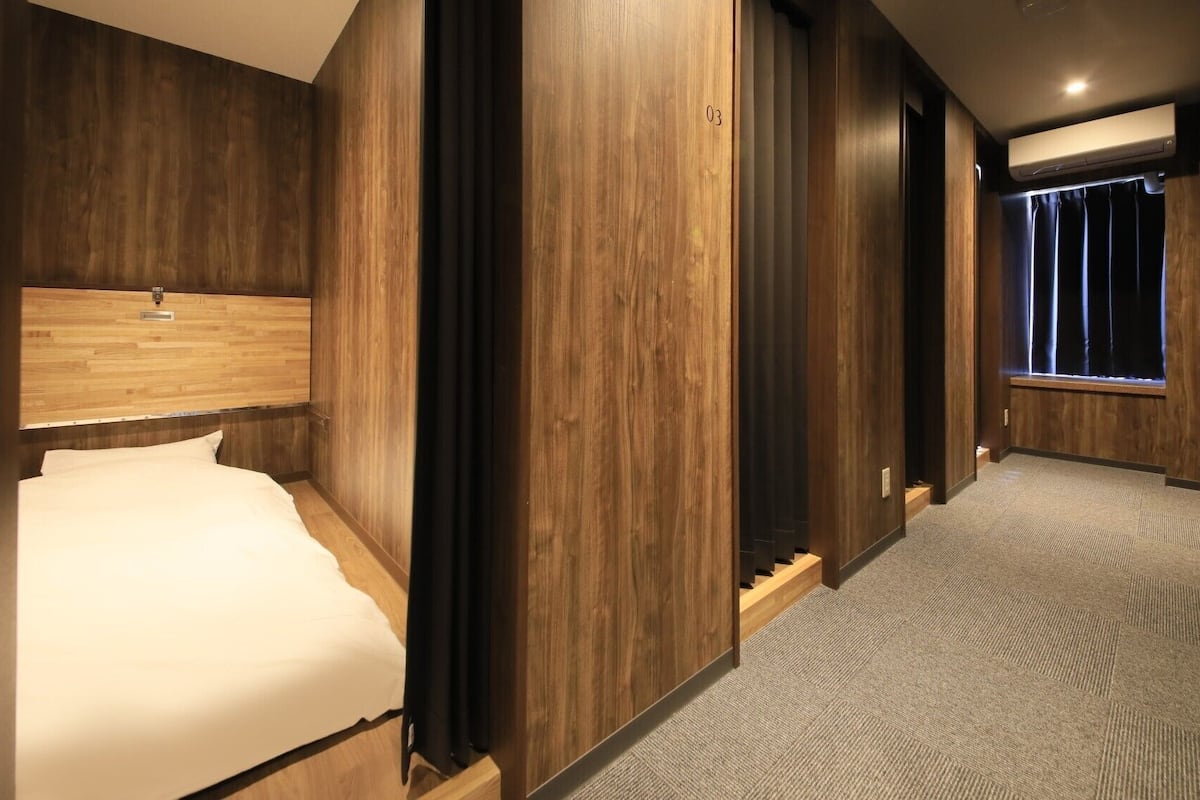 Une chambre d’hôtel avec une tête de lit en bois, un lit, un couloir recouvert de moquette et une fenêtre avec des rideaux.