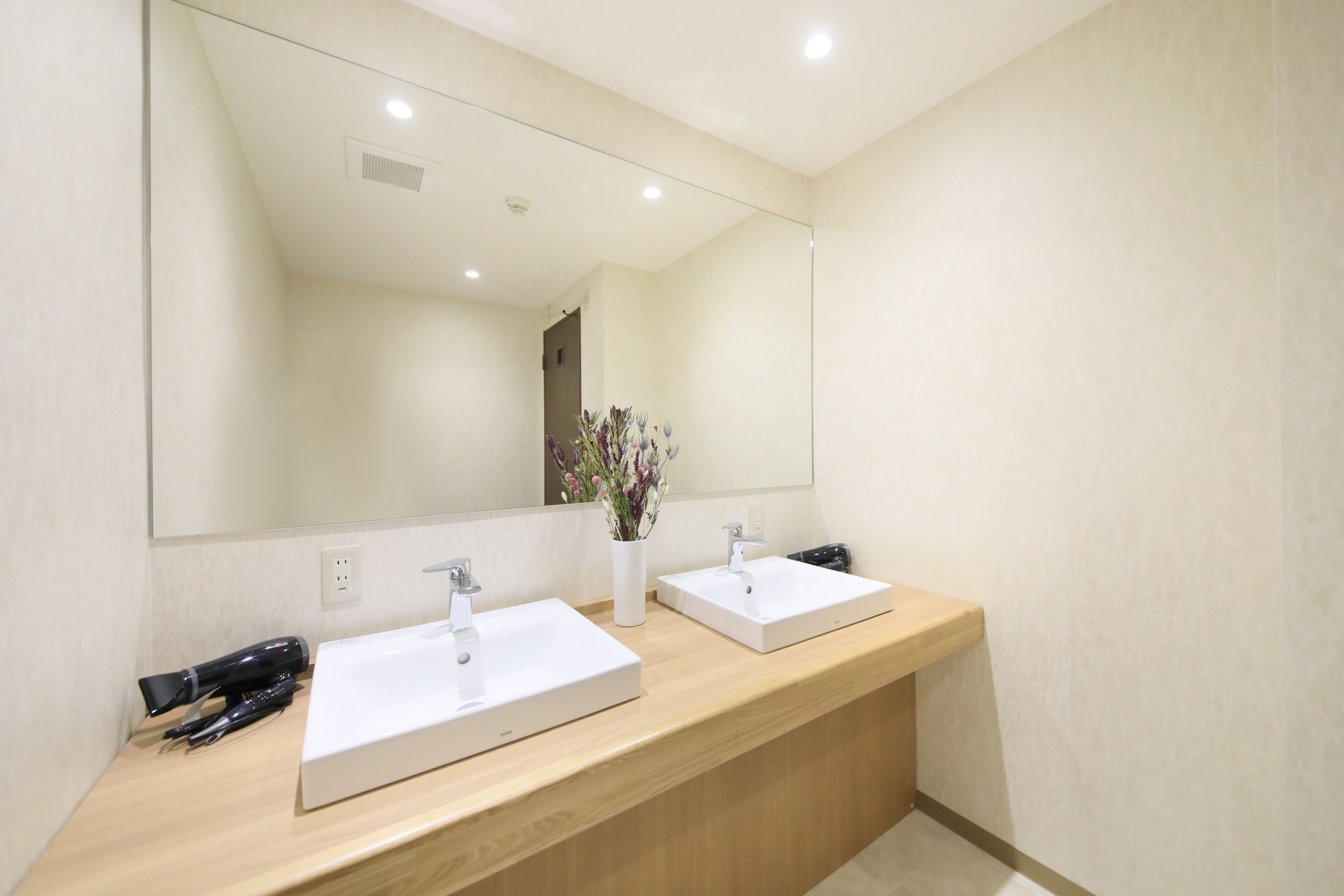 Un baño con dos lavamanos, un espejo y un jarrón con flores.