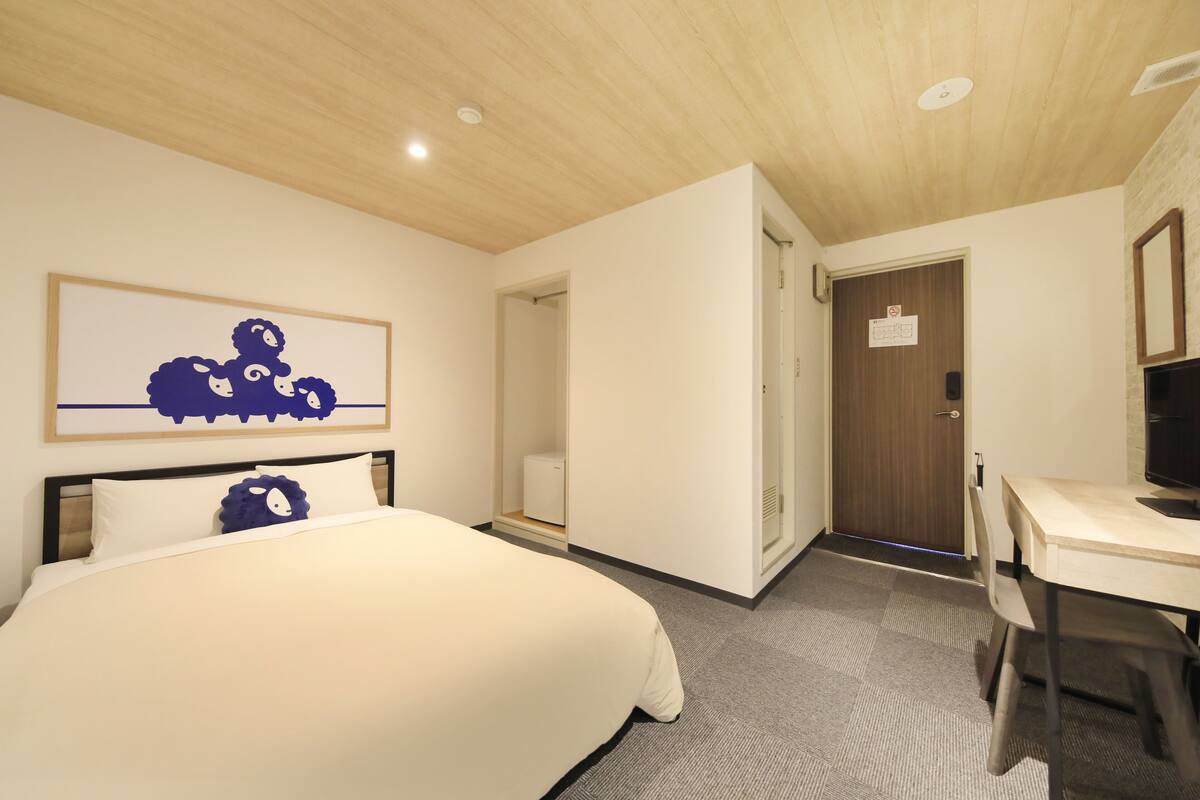 A hotel room with a bed, a desk, a chair, a wooden ceiling, and a door.