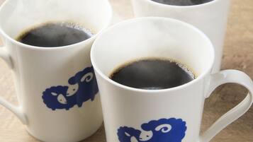 Three white ceramic mugs with blue sheep designs, each containing a dark liquid, likely coffee, on a wooden surface.